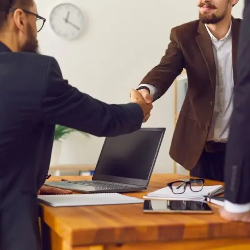 Deux hommes d'affaires se serrent la main au-dessus d'un bureau.
