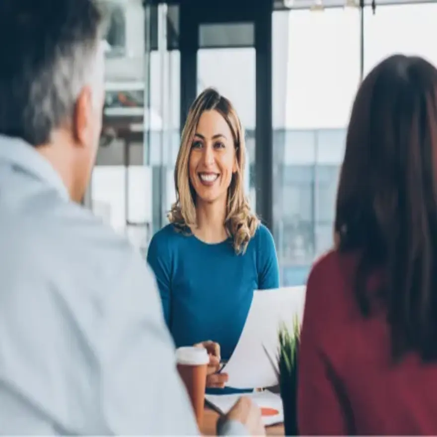 Une femme discute avec deux personnes lors d'une réunion, tous trois attentifs et engagés dans la conversation