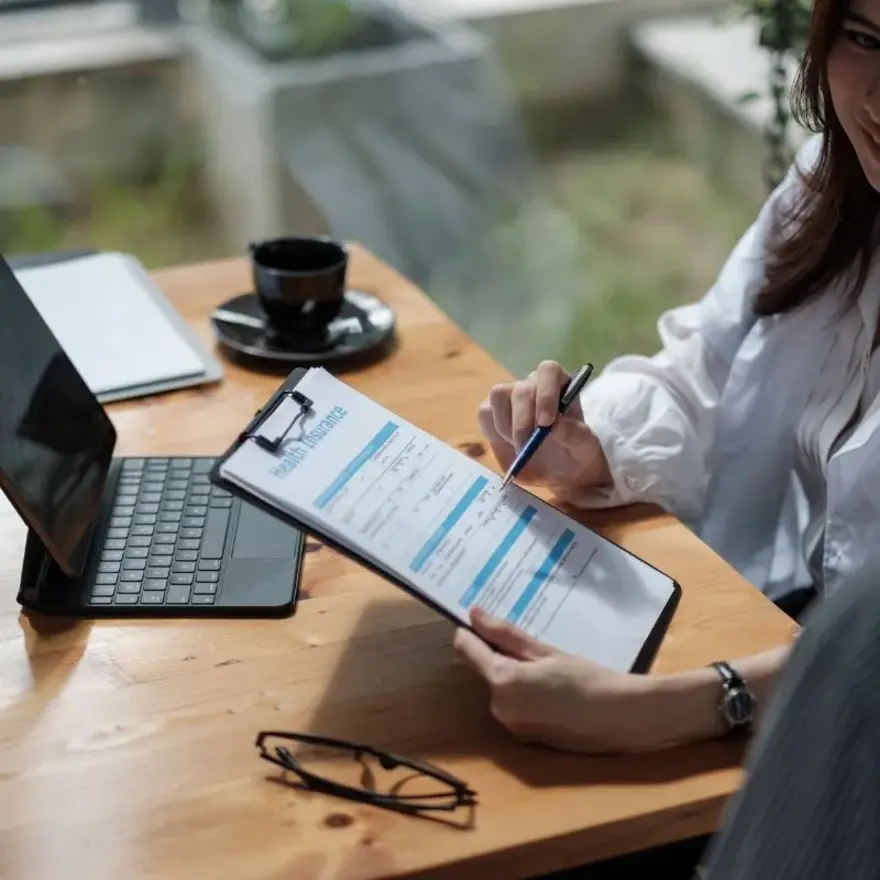 Une femme écrit sur un clipboard en étant assise à une table.