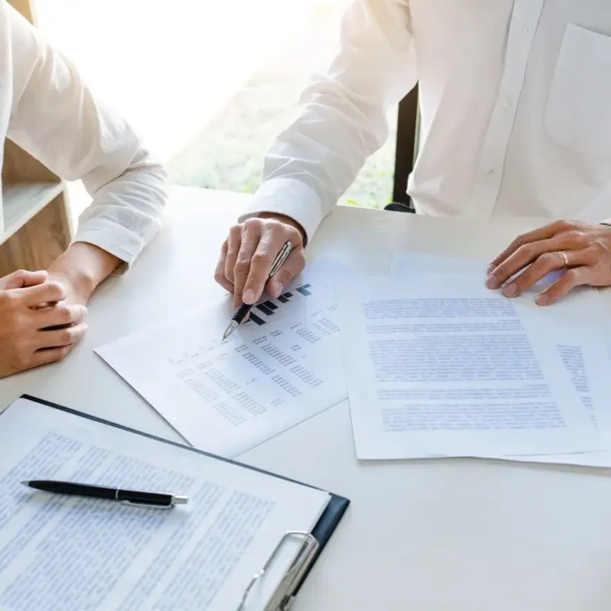 Deux personnes assises à une table, entourées de papiers et de stylos.