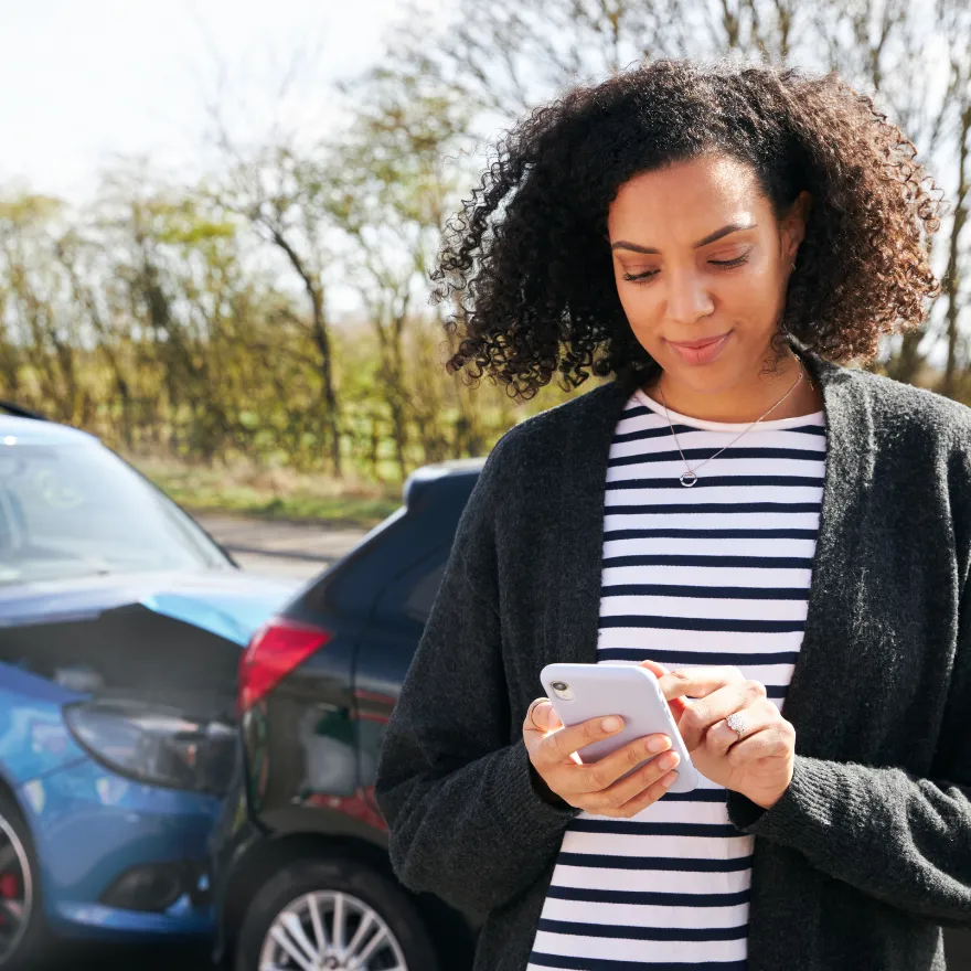Femme regardant son téléphone après un accident de voiture, visiblement préoccupée et en attente d'aide