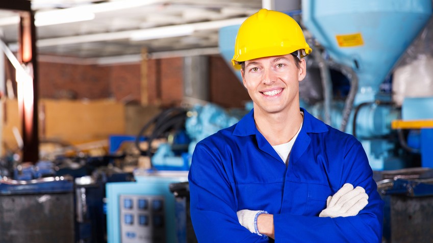Un homme souriant dans une usine, les bras croisés, dégage une attitude confiante et positive