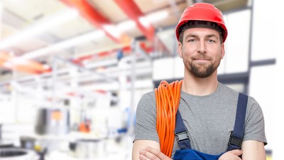 Un homme en salopette et casque se tient devant un entrepôt, prêt à travailler dans un environnement industriel