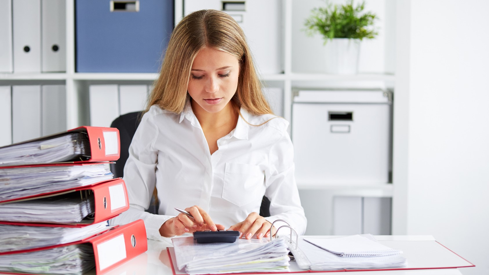 Une femme assise à un bureau, entourée d'une pile de documents à traiter