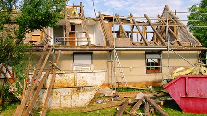 Une maison avec un toit en cours de démolition, des débris tombent autour de la structure
