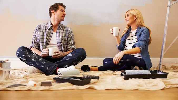 Un homme et une femme assis par terre entourés de pots de peinture, prêts à commencer un projet artistique