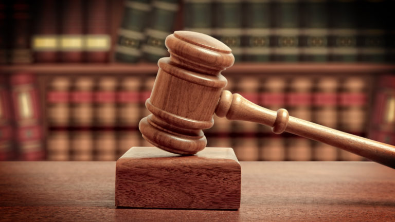 Maillet de juge posé sur un bloc en bois, avec des livres en arrière-plan, symbolisant la justice et le droit