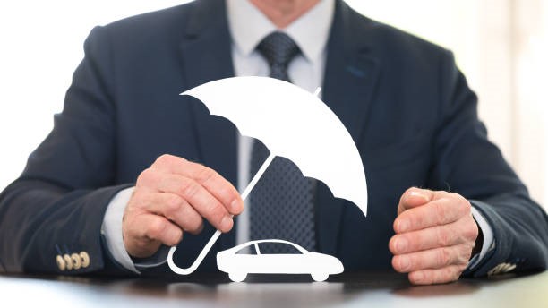 Un homme d'affaires tient un parapluie au-dessus d'une voiture, protégeant ainsi le véhicule de la pluie