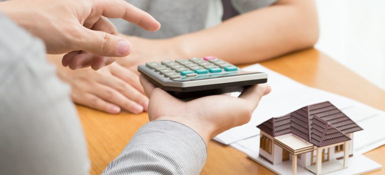 Un homme tient une calculatrice et un modèle de maison, symbolisant la planification financière pour l'achat immobilier