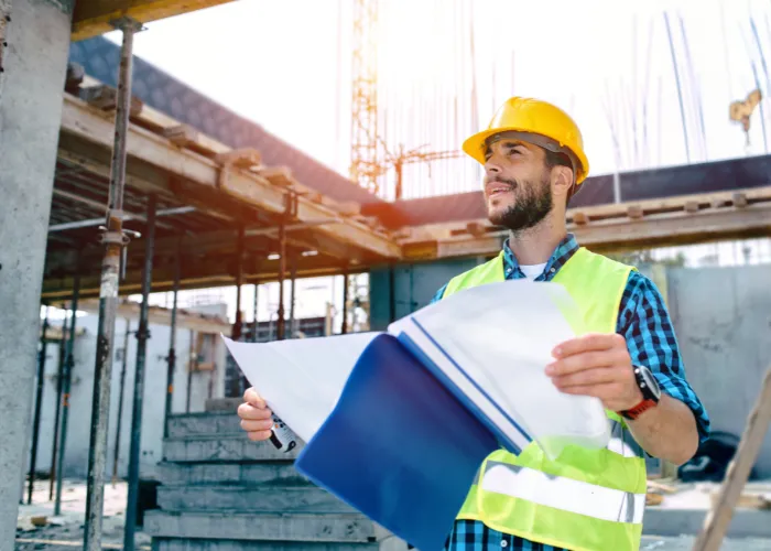 Un homme avec un casque de sécurité présente un dossier bleu, représentant une activité liée à la construction ou à la gestion de projet