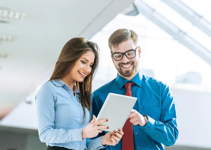 Deux professionnels se tenant dans un bureau, examinant un tableau numérique ensemble