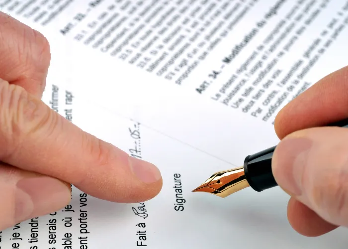 Une personne signe un document avec un stylo, illustrant un acte officiel ou un accord important